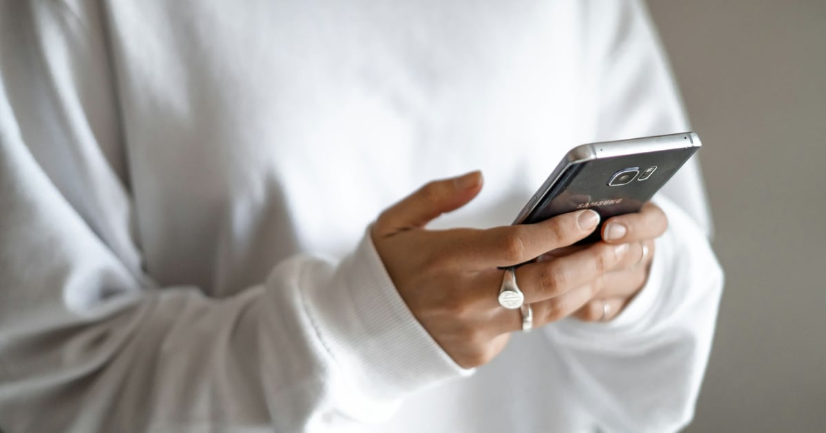 A person in a white sweater holding a smartphone in both hands, scrolling with a thumb