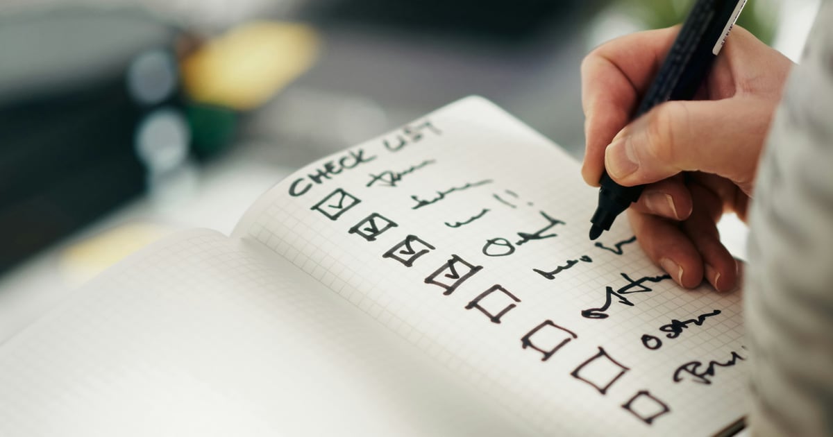 A hand writing in a notebook, ticking boxes down a handwritten checklist, with several boxes still empty