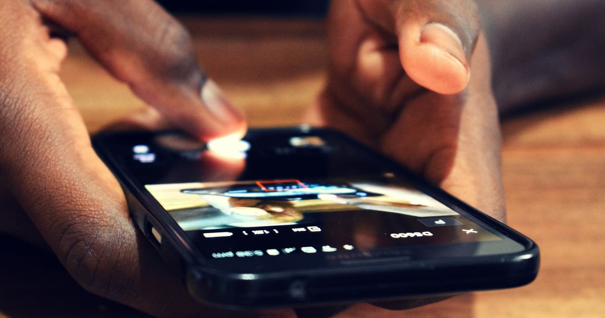 Two hands holding a smartphone flat, one finger tapping the lit screen