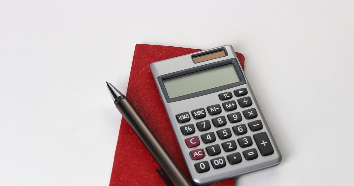 A silver desk calculator and a pen resting on a red notebook against a white background