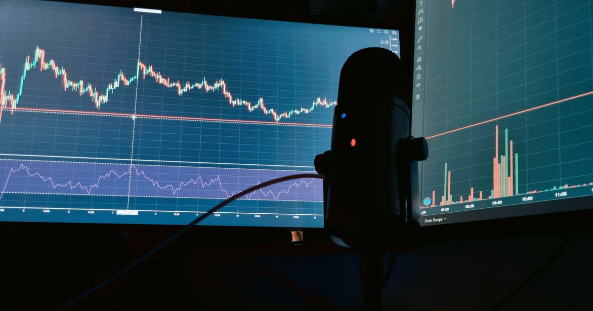 Two monitors showing a jagged line chart and a volume panel, with a microphone silhouetted in front of them