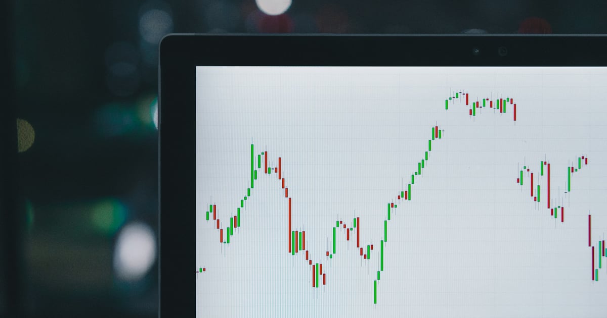 A candlestick chart on a laptop screen at night, sharp in the center and fading into dark blur at the edges
