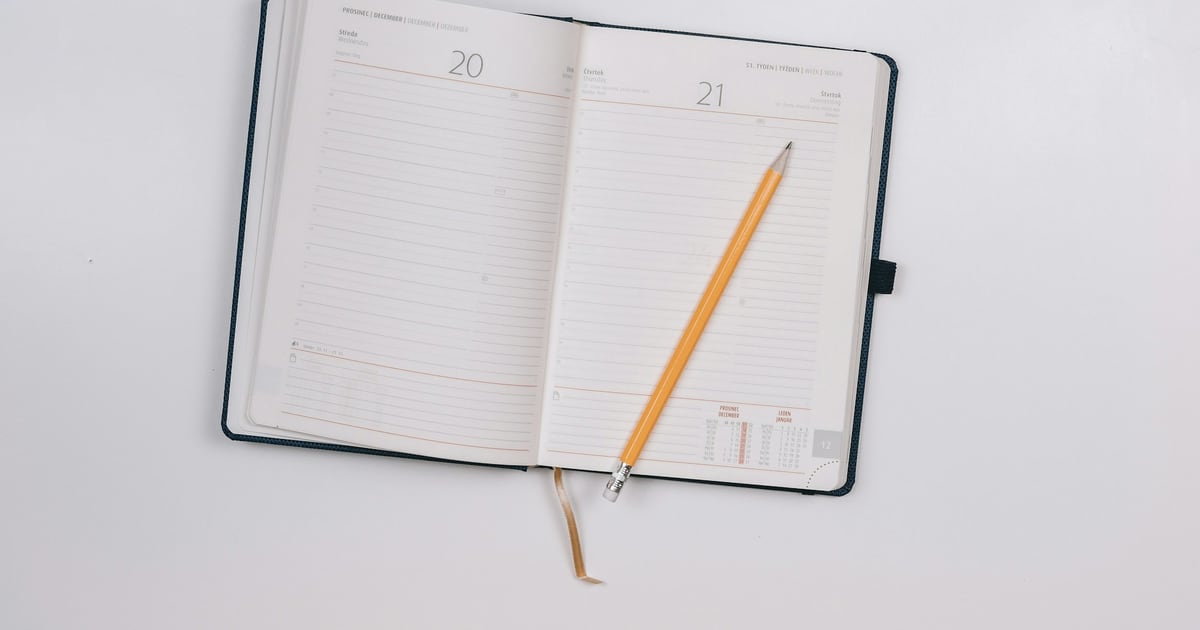 An open diary with two ruled pages for consecutive days and a yellow pencil lying across it